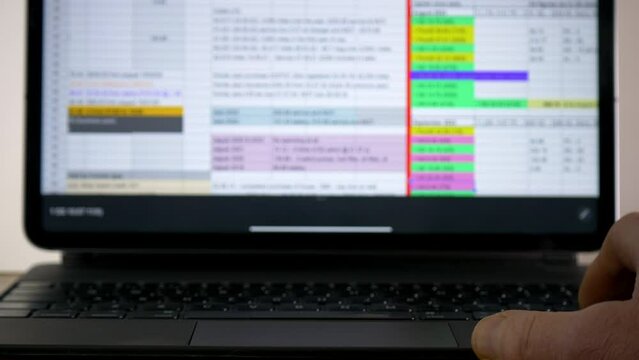 Closeup of a hand using a laptop or tablet keyboard to scroll through data in a spreadsheet app on a screen display.