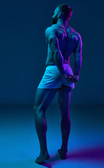 Full length photo. Rear view of young, fit naked man demonstrated his perfect and healthy back shape in neon light against gradient background. Concept of beauty and fashion, art, aesthetic of body.