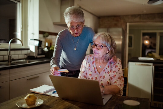 Senior lesbian couple using credit card on laptop at home