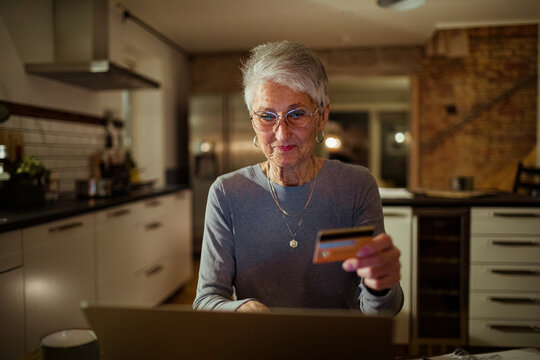 Senior Woman Holding Credit Card With Laptop On Desk At Home