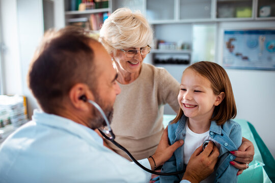 Pediatrician using stethoscope on child with grandmother at clinic