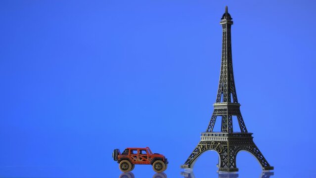 Miniature replica of the Eiffel Tower with a moving toy car against a blue background. 