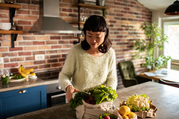 Japanese woman unpacking bought vegetables in home kitchen