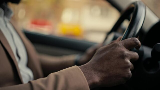 Close-up shot of a man Businessman with Black skin color in a brown jacket holds with his two hands the steering wheel of a modern car while he is driving in a car in a modern salon during a business