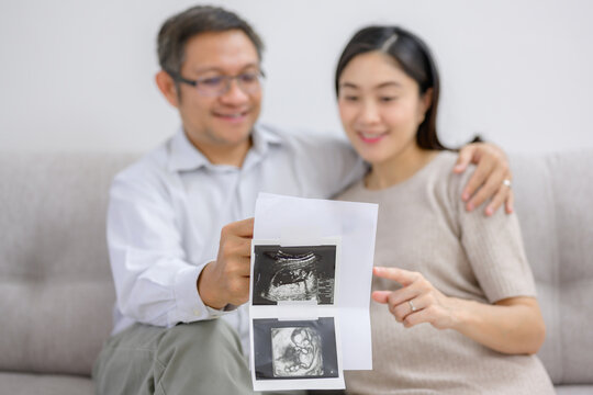 A pregnant woman and husband Asian couple looking at ultrasound images of their child Happy pregnant woman in the living room of her home before giving birth