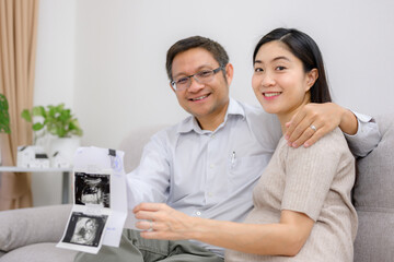 A pregnant woman and husband Asian couple looking at ultrasound images of their child Happy pregnant woman in the living room of her home before giving birth