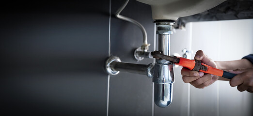 Plumber uses wrench to repair water pipe under sink There is maintenance to fix the water leak in the bathroom.with red wrench, plumbing install concept. - obrazy, fototapety, plakaty