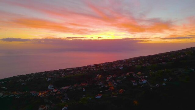Aerial establishing shot of village on hill of Madeira with ocean view during orange sunset 