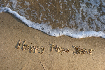 Happy New Year word hand written on the sand beach in summer with waves and white foam on the top