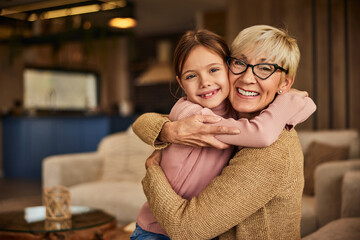 A portrait of a cute little girl and her grandma in a hug, spending the day at home.