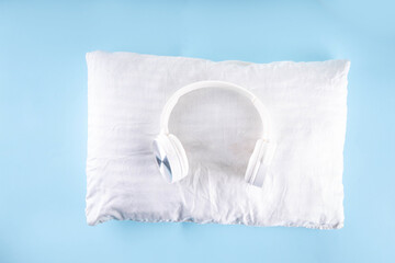 Sonic Hues and Noise for sleep concept with comfortable headphones and white pillow on light blue background top view copy space