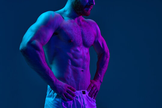 Portrait of young msn with athletic body put hands on his hips while posing in underwear in neon light against gradient background. Concept of beauty and fashion, art, aesthetic of body, masculinity.