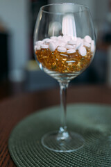 Round tablets of light pink color in a glass and transparent capsules of yellow color. Taking vitamins to improve health and well-being. Dietary supplements on the recommendation of a doctor