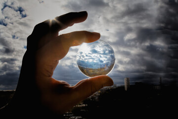 A hand holds a lens on which light falls and reflects a cityscape