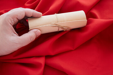 A hand holds a gift wrapping tied with a rope, red fabric background, a gift for the holiday