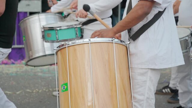 A group of drummers playing rhythmic sambo music during a carnival procession close-up dressed in white traditional suits.