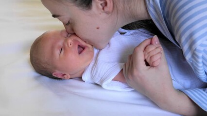 Portrait of a crying newborn baby. A young mother holds the baby by the hands, kisses and soothes him. Mental Health in Postpartum Time. Pregnancy And Depression.