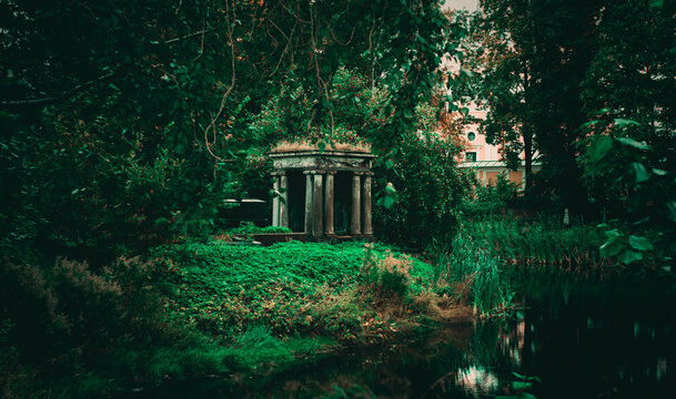 In the overgrown green garden there is an old stone crypt on a summer evening. Dense thickets of plants and medieval architecture.