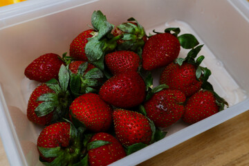 strawberries in a plastic container on a wooden table