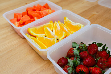 plastic containers containing papaya, strawberries and oranges, on a wooden background
