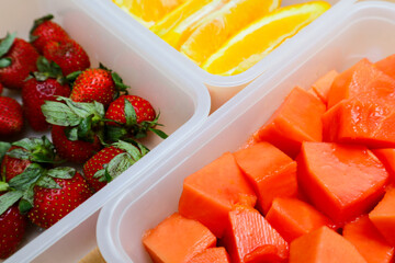plastic containers containing papaya, strawberries and oranges, on a wooden background