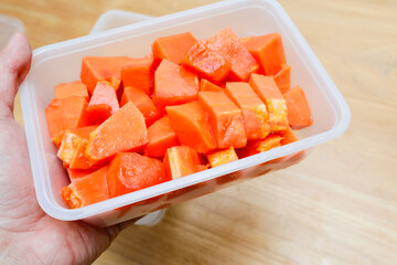 papaya fruit that has been cut into small pieces in a plastic container on a wooden table