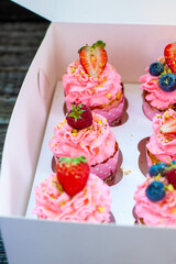 Festive pink cupcakes with fresh strawberries, raspberries and blueberries on cardboard box with chopped pistachios on the top
