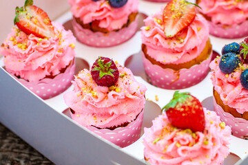 Festive pink cupcakes with fresh strawberries, raspberries and blueberries on cardboard box with chopped pistachios on the top