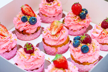 Festive pink cupcakes with fresh strawberries, raspberries and blueberries on cardboard box with chopped pistachios on the top