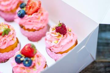 Festive pink cupcakes with fresh strawberries, raspberries and blueberries on cardboard box with chopped pistachios on the top