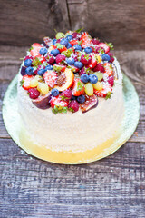 Coconut cake with a pile of fresh peaches, apples, raspberries, blueberries and nuts on wooden background
