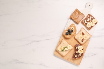 Toasts with different nut butters, fruits and nuts on white marble table, flat lay. Space for text