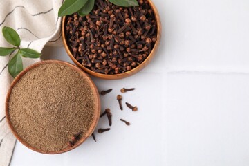 Aromatic clove powder and dried buds in bowls on white tiled table, flat lay. Space for text