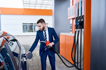 Side view portrait of elegant businessman refueling luxury car at gas station, copy space