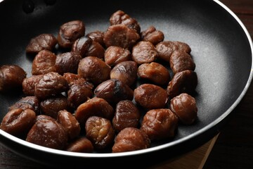 Roasted edible sweet chestnuts in frying pan on table, closeup