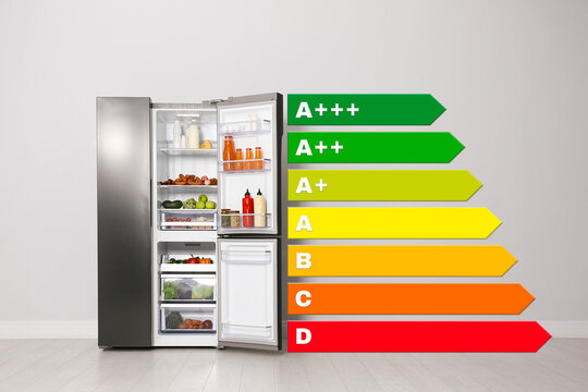 Energy efficiency rating label and open refrigerator near light wall indoors