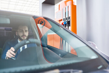 Portrait of modern businessman sitting behind the wheel of luxury car in gas station