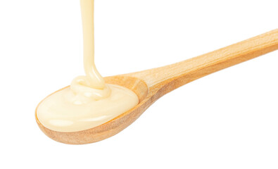 pouring condensed milk in wooden spoon isolated on white