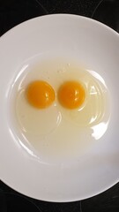 Preparing for omlette cooking with two raw eggs in a white plate.