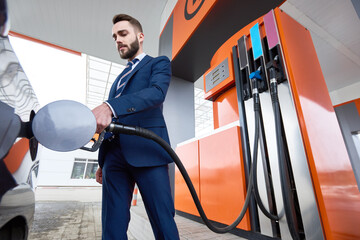 Low angle shot of successful businessman refueling gas tank of luxury car in petrol station - obrazy, fototapety, plakaty