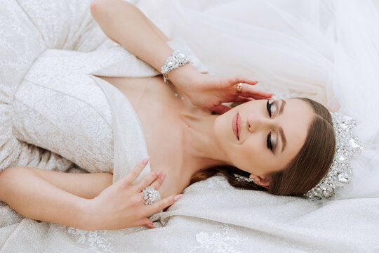 A beautiful bride in a white dress is lying. A girl in a white dress is resting. Beautiful hair and makeup. The model poses for the photographer.