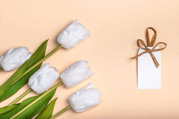Blank tag on a peach background with white tulips. Congratulations concept for Easter, International Women's Day, Mother's Day, Valentine's Day and Birthday.
