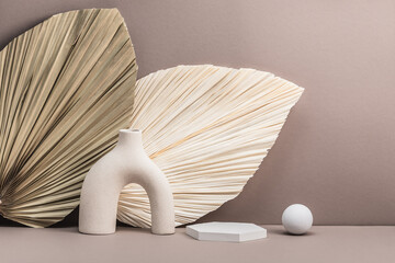 Beige-brownish background with dry palm leaves and ceramic vase. Empty plaster showcase for the...