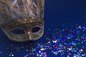 Golden Mardi Gras or carnival face mask  on a dark blue background with colored tinsel and...