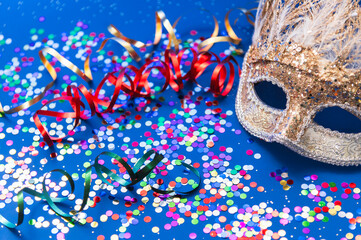 Golden Mardi Gras or carnival face mask on a blue background with colored tinsel and confetti....