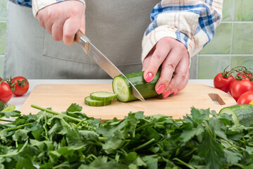 Vegetables with herbs and female hands cutting a cucumber into a salad.