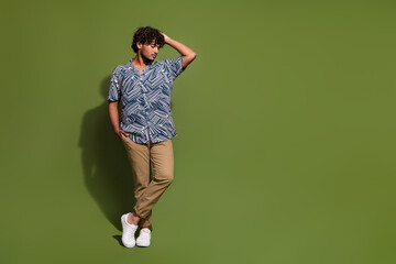 Fototapeta na wymiar Full length photo of young confident latin man macho posing touching his curly hair looking empty space isolated on khaki color background