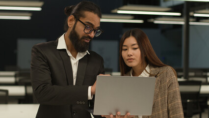 Diverse multiracial colleagues business people in office discussing new online laptop startup project Indian Arabian businessman mentor consult talk to Asian Korean businesswoman partner client help