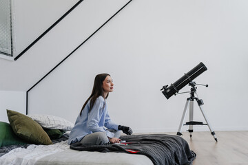 Young woman  with artificial bionic hand with a telescope indoors, looking curious and contemplative