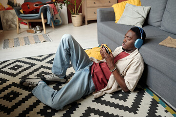 African American guy with smartphone connected to gamepad playing video game at leisure while...